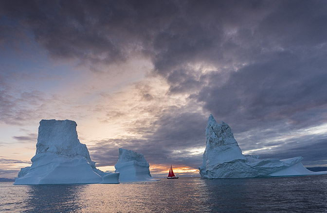 A yacht with red sails cruising between icebergs at dusk, 2017